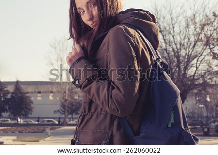 Back to school student girl looking to side in park wearing backpack. Female university college student looking at camera in park. Beautiful young long haired woman