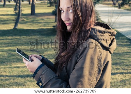 Young girl posing outdoors with tablet PC in her hands and look back. Toned colorized image, film like color.