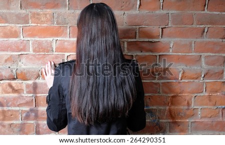 Back view of long haired brunette women against red brick wall.