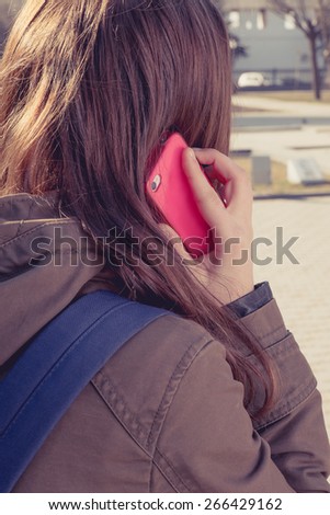 Rear view of brunette girl call by red cell phone outdoors. Closeup image.