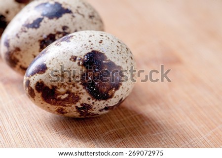 Three organic quail eggs on wooden background macro.Spotted quail eggs on wooden plate, image with copyspace.Lit from the side Quail eggs is well known as source of protein, vitamins and microelements