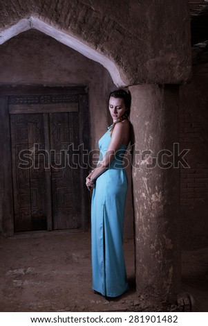 Women in long blue dress posing leaning old column  toned image