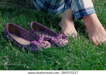 Barefoot women sitting on grass cross legged and her shoes near, a lot of copyspace