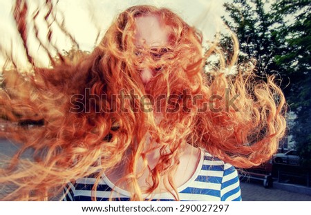 Portrait of a beautiful redhead girl with flying hair in the wind outdoors. Young casual girl with wavy hair