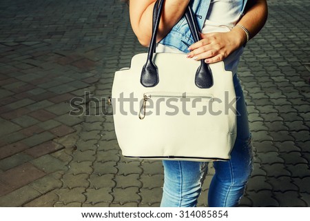 Women with fashionable handbag. Beautiful fashion woman wear vintage tight jeans, white hand bag and denim jacket. Toned in warm colors. Outdoors shot, lifestyle.
