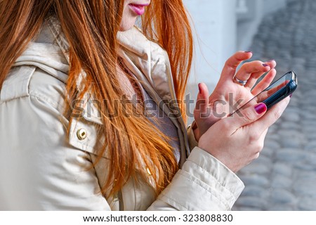 Closeup of redhair girl texting on mobile phone,closeup of the hands holding mobile device. red haired woman holding smart phone, phablet of small digital tablet in hands and using mobile internet app