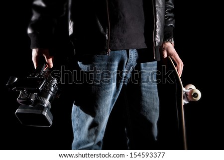 Skateboarder Holding a video camera and a skateboard isolated on black background