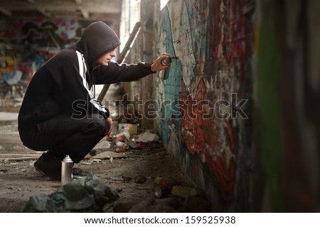 Illegal Young man Spraying black paint on a Graffiti wall. (room for text)