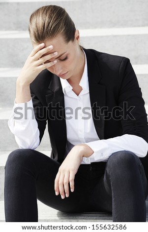 Young businesswoman sitting on steps with head in hands