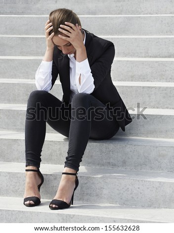 Young businesswoman sitting on steps with head in hands