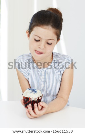 Young girl holding cup cake, licking lips