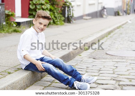 Young boy sitting on curb, smiling