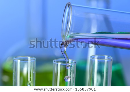 Liquid pouring into test tube from graduated cylinder in laboratory