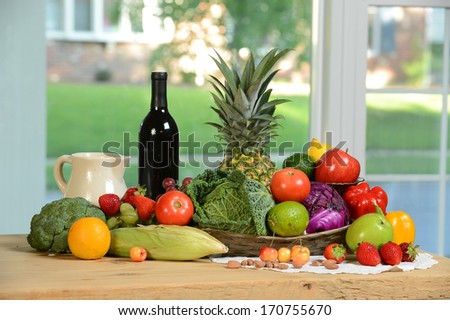A basket of fresh fruits and vegetables with red wine on wood table