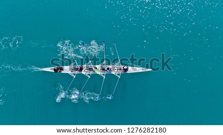 Aerial drone bird\'s eye view of sport canoe operated by team of young women in deep blue sea waters