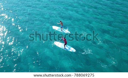 Aerial drone bird\'s eye view of 2 men exercising sup board in turquoise tropical clear waters