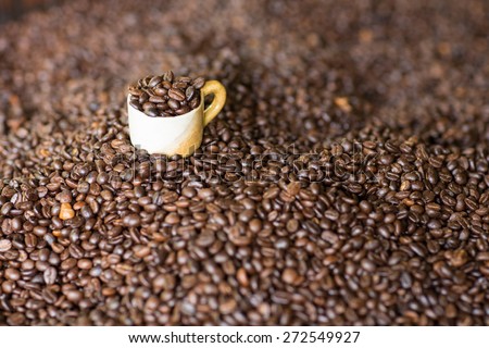 Cup filled with coffee beans on top of a pile of roasted coffee bean