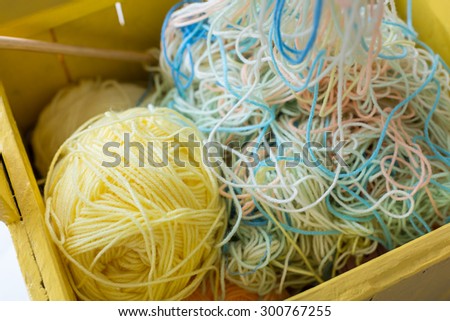 Colorful yarns and yarn balls in yellow wooden bucket.
