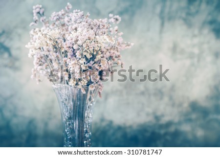 Dry flower in tall and transparent vase with old cement wall in the background in retro looks.