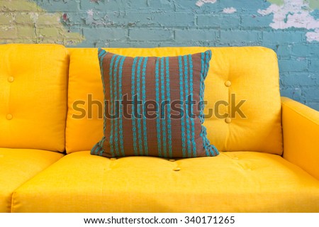 Close up of yellow fabric sofa and cushions with vintage style against blue bricks wall.