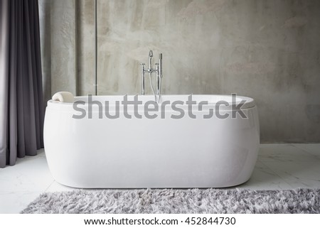 Big white bathtub in a middle of industrial loft bathroom style with grunge cement wall.