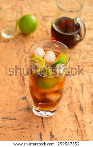 Rum and Coke Cocktail Drink with Lime Wedges on Wood Background
