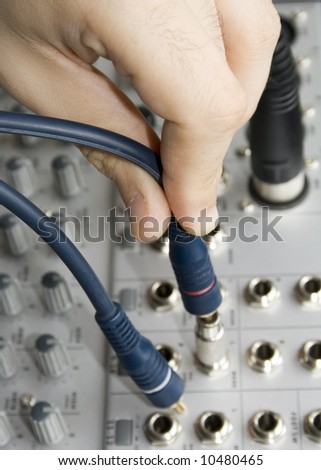 Close up macro o a hand plugging a plug in a mixer board.