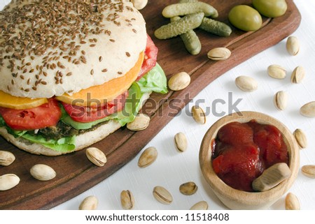Close up of a vegetarian burger made from lentils and azuki beans, with tomato baked pumpkin slices and lettuce in a whole-grain bread with flax seeds. Focus is at the front.