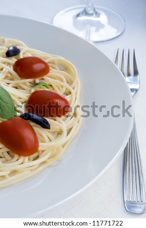 View of one half of a spaghetti dish with cherry tomatoes, black olives and basil.