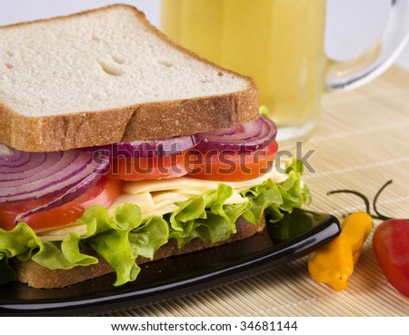Vegetarian sandwich close up, with cheese, lettuce, tomato and onion in white bread. A glass of clod beer on the background.