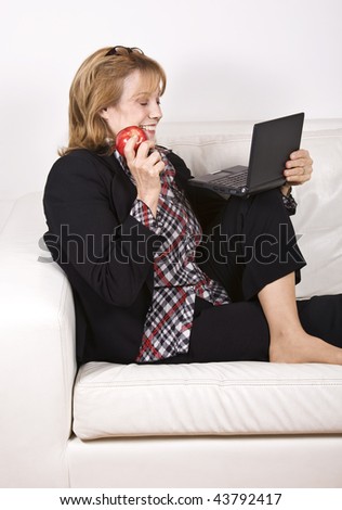A senior woman eating an apple comfortably sitting in her livingroom with a laptop. An apple a day keeps doctors away.
