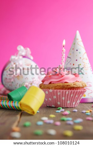 Birthday cupcake with candle and birthday hats in background