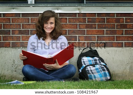 Smiling girl sit on a grass and study her lessons