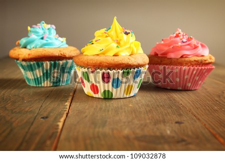 Three different colors cupcakes on a wooden table, blue, yellow and pink.
