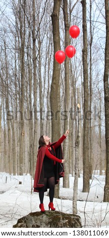woman holding a bunch of red balloons in a forest