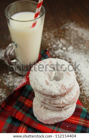 Stack ot three ice sugar powdered donuts on a red tablecloth and a glass of fresh milk