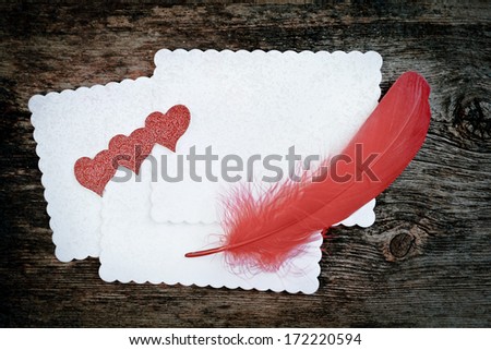 Blank white paper with red feather and hearts on it.  Wooden background.