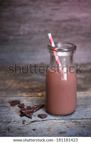 Old-fashioned bottle of chocolate milk with red striped straw and fresh dark chocolate on wooden background