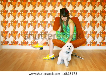 teenager sit in an orange chair with white dog and having vintage wallpaper in background