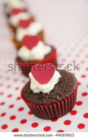 Row of cup cakes with white frosting and red heart on top