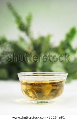 Single clear cup with jasmine tea with herb in background