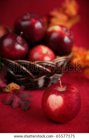 Red apple with heart shape on the apple and a basket full of red apples