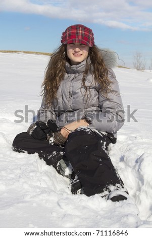 Teen with a grey jacket and red cap sit in snow by a nice winter day