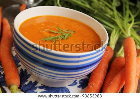 Carrot soup in a blue bowl with fresh carrot on side