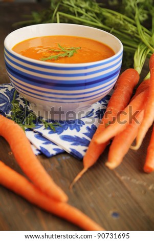Carrot soup in a blue bowl with fresh carrot on side