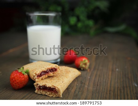 Organic cereal bar with fruit filling and fresh raspberry on a wooden table with a glass of milk