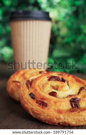 Sweet buns with raisin and a coffee to go on a table for breakfast