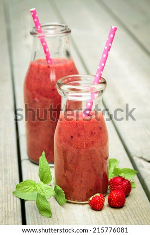 Strawberry smoothie freshly made in a jar with a pink straw on rustic wood