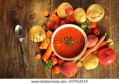 Vegetables soup surrounded by fresh vegetables and a spoon on a wooden background