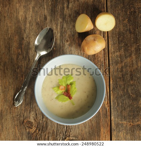 Top view of a potato soup in a blue bowl with fresh potatoes and spoon on a wooden background